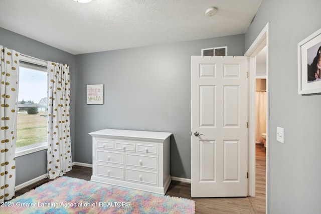 bedroom featuring light wood finished floors, visible vents, a textured ceiling, and baseboards