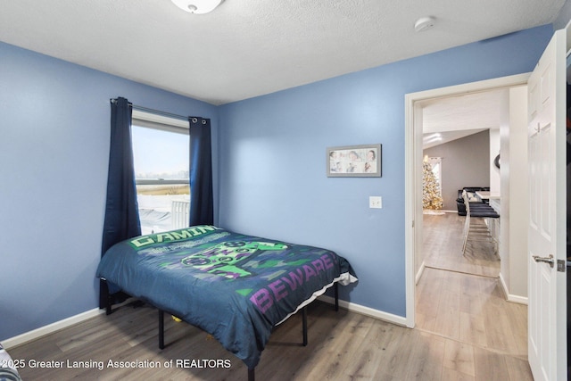 bedroom with a textured ceiling, light wood-type flooring, and baseboards