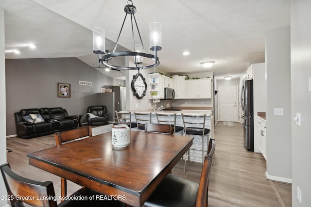 dining room with light wood-type flooring, baseboards, visible vents, and vaulted ceiling