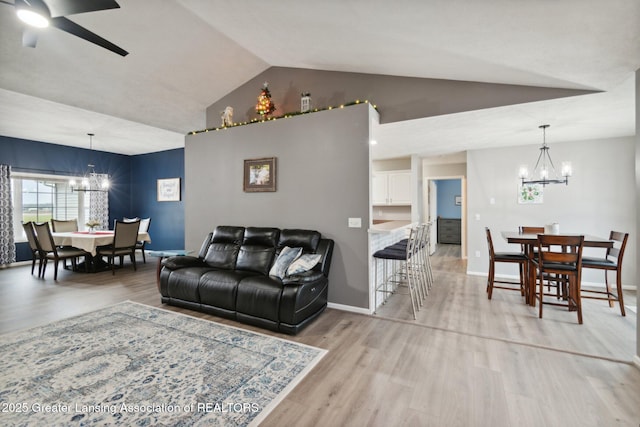 living room with ceiling fan with notable chandelier, baseboards, light wood-style floors, and vaulted ceiling