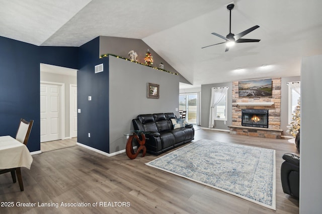 living area with visible vents, a ceiling fan, wood finished floors, a stone fireplace, and baseboards