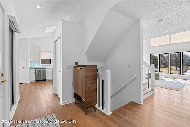 stairway with lofted ceiling, a textured ceiling, wood finished floors, recessed lighting, and baseboards