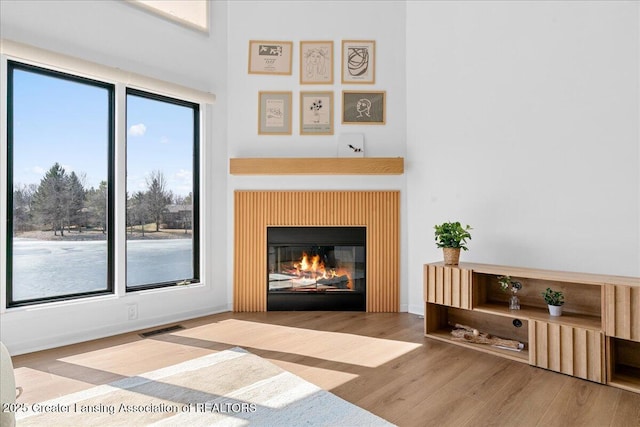 living room with a glass covered fireplace, wood finished floors, and visible vents