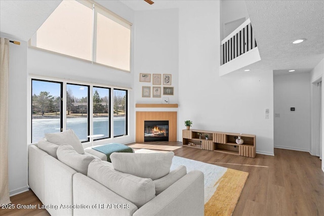 living room with a fireplace with flush hearth, wood finished floors, baseboards, and a textured ceiling