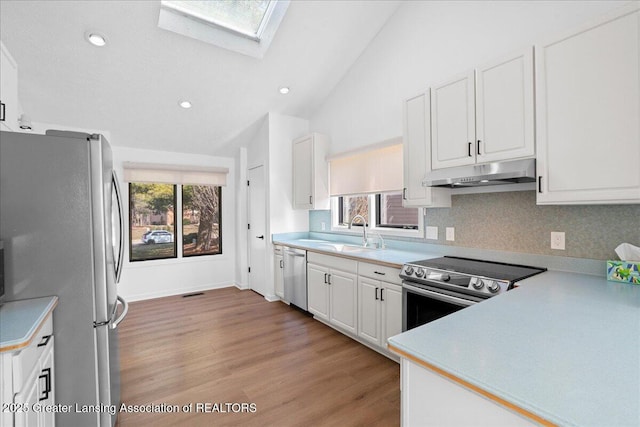 kitchen with lofted ceiling with skylight, under cabinet range hood, a sink, white cabinetry, and appliances with stainless steel finishes