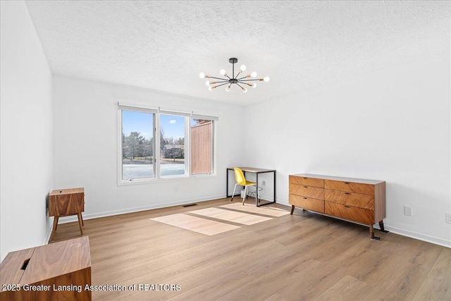 interior space with baseboards, a textured ceiling, an inviting chandelier, and wood finished floors