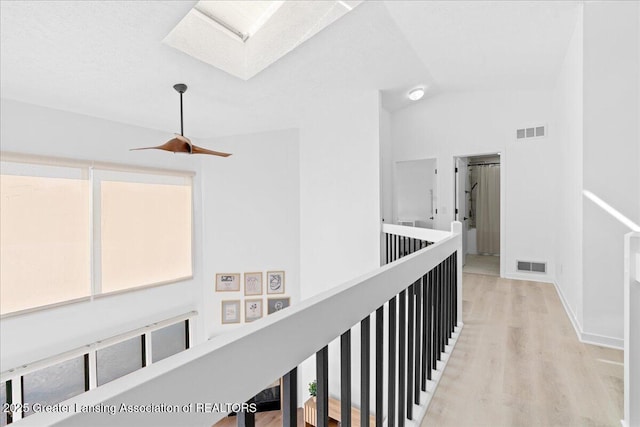 hall with vaulted ceiling with skylight, baseboards, visible vents, and light wood-type flooring