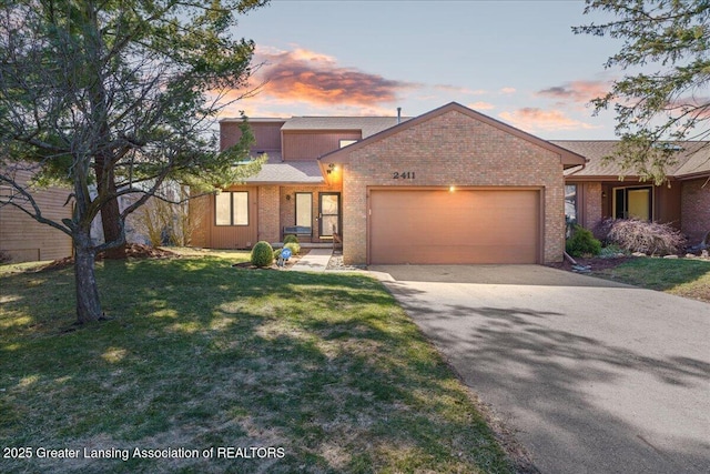 view of front of house featuring aphalt driveway, a yard, brick siding, and a garage