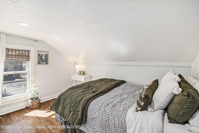 bedroom with hardwood / wood-style floors, lofted ceiling, baseboards, and a textured ceiling