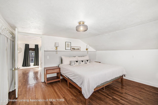 bedroom with baseboards, a textured ceiling, lofted ceiling, and wood finished floors