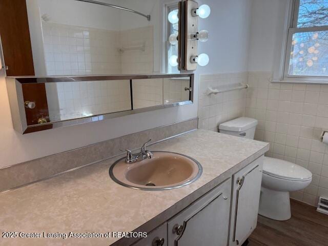 bathroom featuring a wainscoted wall, toilet, wood finished floors, tile walls, and vanity