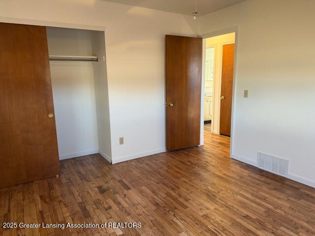 unfurnished bedroom featuring a closet, visible vents, baseboards, and wood finished floors