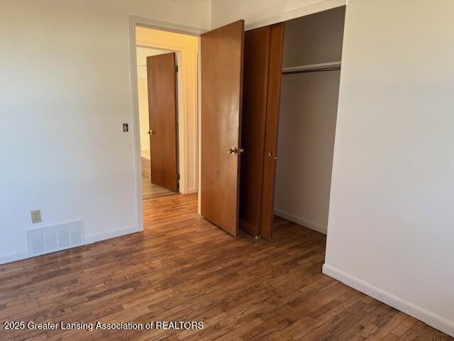 unfurnished bedroom with a closet, visible vents, baseboards, and wood finished floors