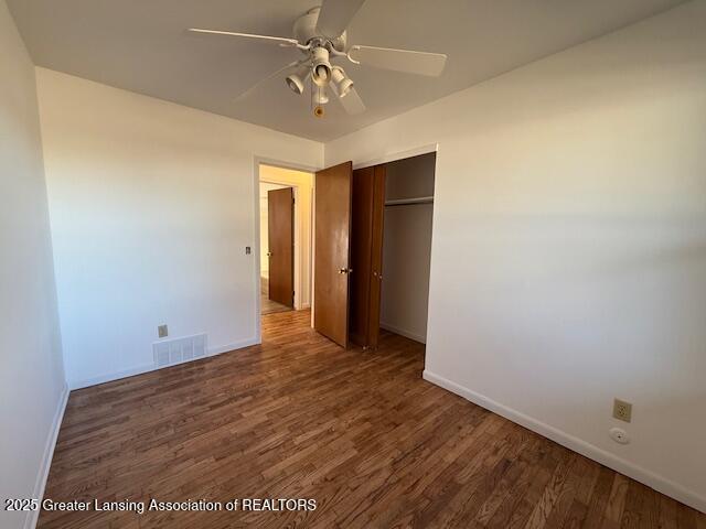 unfurnished bedroom with wood finished floors, visible vents, a closet, and baseboards