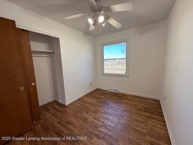 unfurnished bedroom featuring wood finished floors, visible vents, baseboards, ceiling fan, and a closet