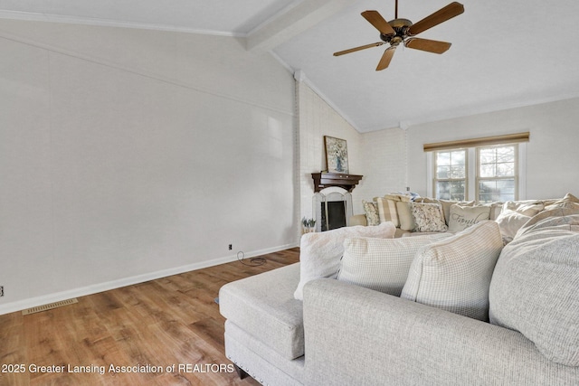 living room featuring wood finished floors, visible vents, baseboards, lofted ceiling with beams, and a brick fireplace