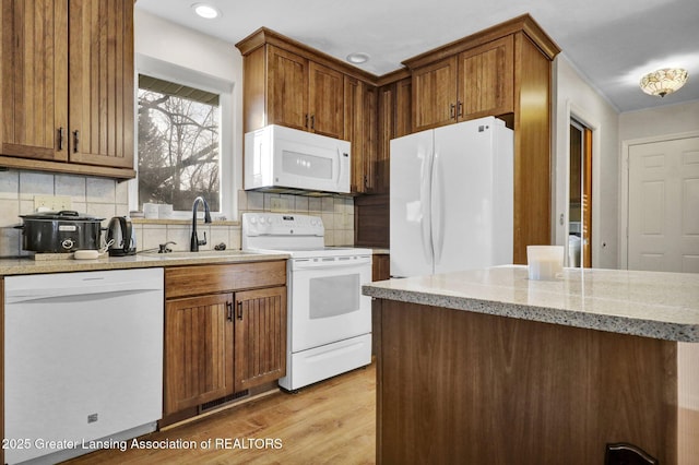 kitchen with white appliances, brown cabinetry, light wood-style flooring, a sink, and decorative backsplash