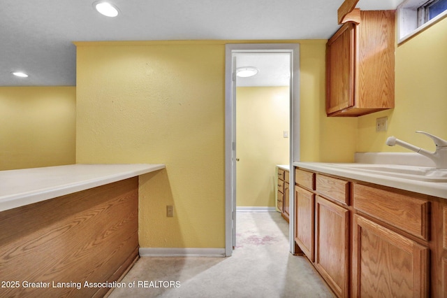 kitchen featuring brown cabinets, a sink, recessed lighting, light countertops, and baseboards