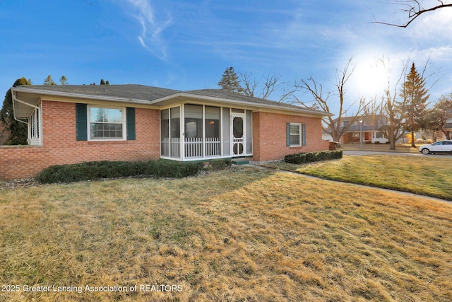 single story home with brick siding, a front yard, and a sunroom