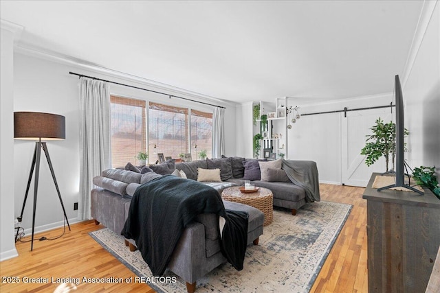 living area with a barn door, baseboards, crown molding, and light wood finished floors