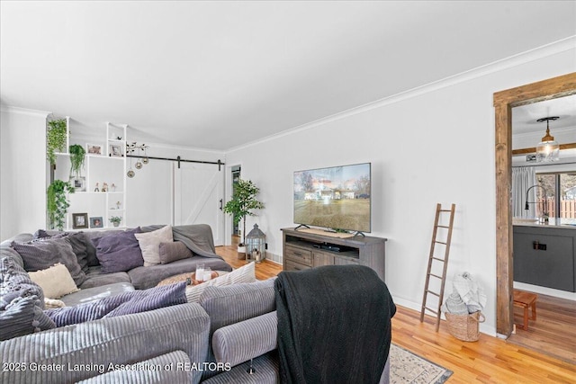 living area with a barn door, light wood-style floors, baseboards, and ornamental molding