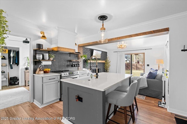 kitchen with stainless steel electric stove, light countertops, light wood-style floors, crown molding, and open floor plan