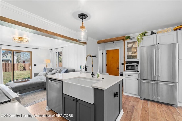 kitchen featuring light wood finished floors, a sink, light countertops, appliances with stainless steel finishes, and crown molding