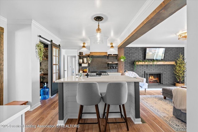 kitchen featuring light countertops, light wood-style floors, crown molding, a brick fireplace, and backsplash