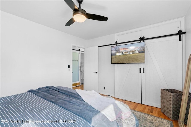 bedroom with a ceiling fan, a barn door, and wood finished floors