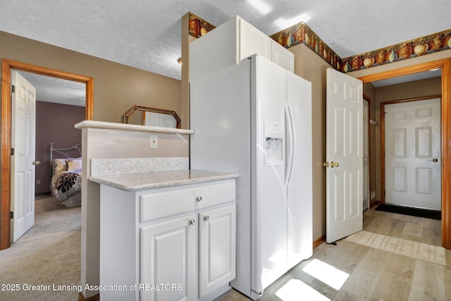 kitchen featuring white cabinetry, light countertops, white fridge with ice dispenser, and a textured ceiling