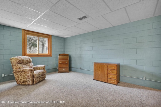 living area with visible vents, a drop ceiling, concrete block wall, and carpet floors