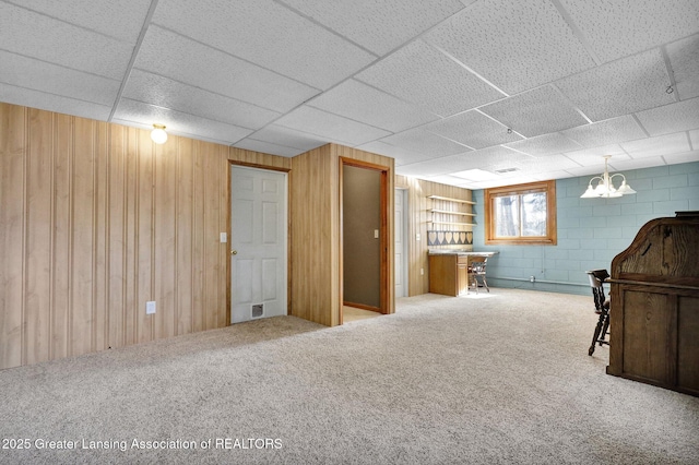 basement with a drop ceiling, concrete block wall, wood walls, and carpet floors