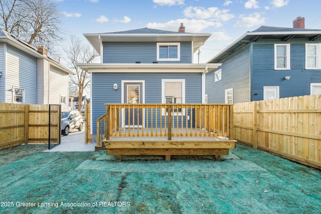 back of house with a chimney, a lawn, a wooden deck, and a fenced backyard