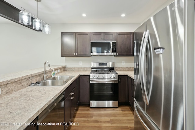 kitchen featuring light wood finished floors, dark brown cabinets, light countertops, appliances with stainless steel finishes, and a sink