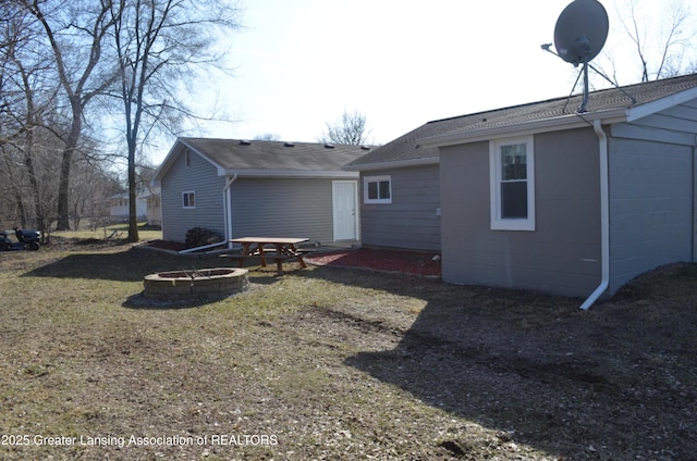 rear view of property featuring a lawn, fence, a fire pit, roof with shingles, and concrete block siding