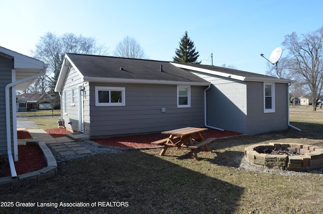 rear view of property with a fire pit, roof with shingles, and a lawn