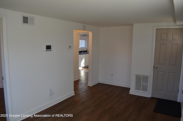 empty room featuring dark wood-type flooring, baseboards, visible vents, and a sink