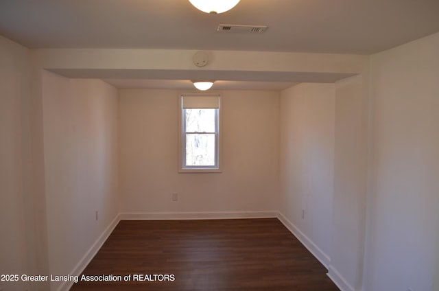 unfurnished room with visible vents, baseboards, and dark wood-style flooring