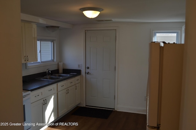 kitchen with dark countertops, electric range oven, freestanding refrigerator, white cabinetry, and a sink