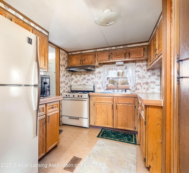 kitchen with white appliances, light floors, wallpapered walls, a sink, and light countertops