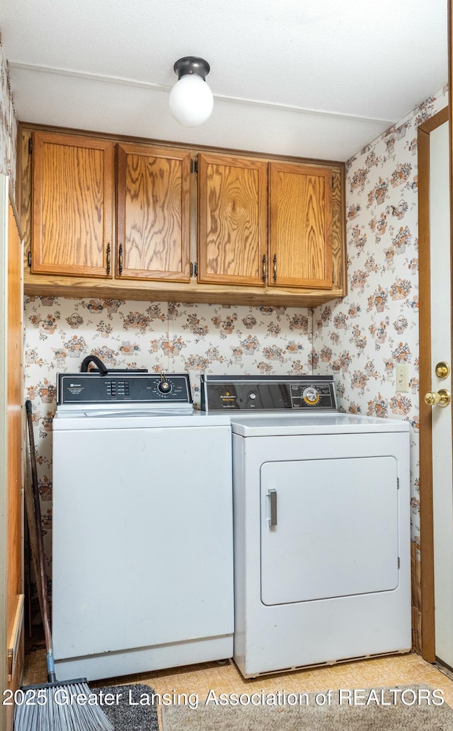 washroom featuring washer and clothes dryer, cabinet space, and wallpapered walls