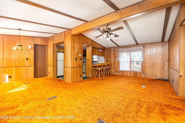 carpeted spare room with vaulted ceiling with beams, a ceiling fan, visible vents, and wood walls