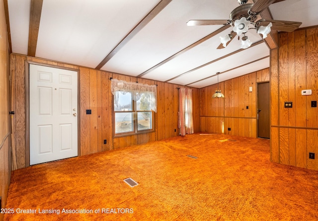 empty room with visible vents, carpet, wood walls, and vaulted ceiling with beams