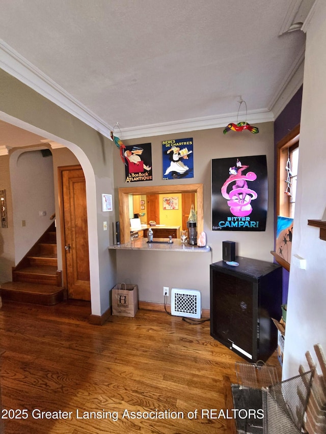 unfurnished living room with stairway, arched walkways, wood finished floors, and crown molding