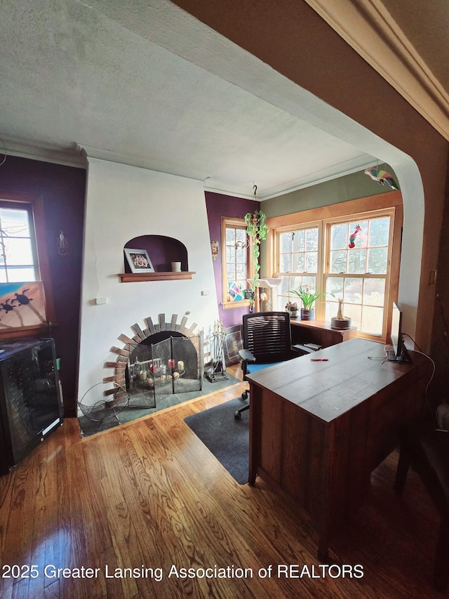 home office featuring a textured ceiling, a brick fireplace, wood finished floors, and a healthy amount of sunlight