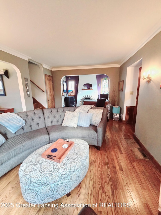 living area featuring baseboards, arched walkways, wood finished floors, and ornamental molding