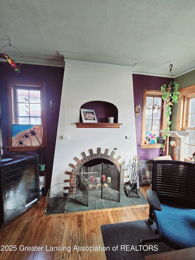 living area featuring plenty of natural light, a brick fireplace, wood finished floors, and crown molding