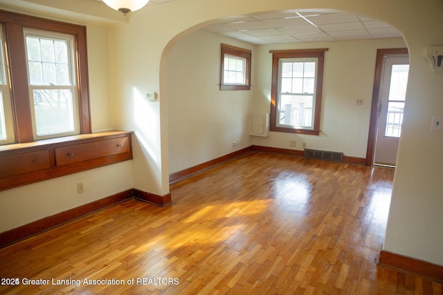 unfurnished room with arched walkways, visible vents, light wood-type flooring, and baseboards