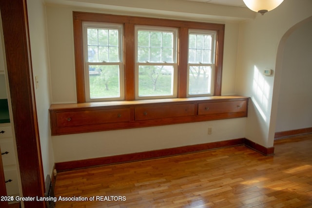 spare room featuring light wood-type flooring, arched walkways, and baseboards