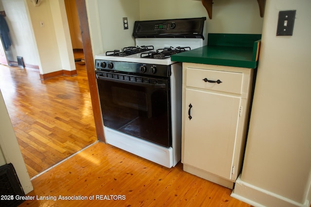 kitchen featuring baseboards, gas range, white cabinetry, and light wood finished floors